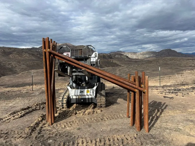 Prefabricated steel pipe fence braces standing upright on a job site in front of a tracked skid steer